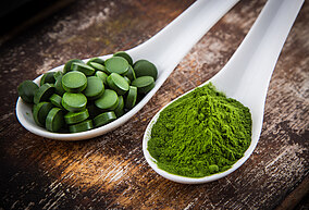 Ein Löffel mit Chlorella in Tablettenform und ein Löffel mit Chlorella in Pulverform