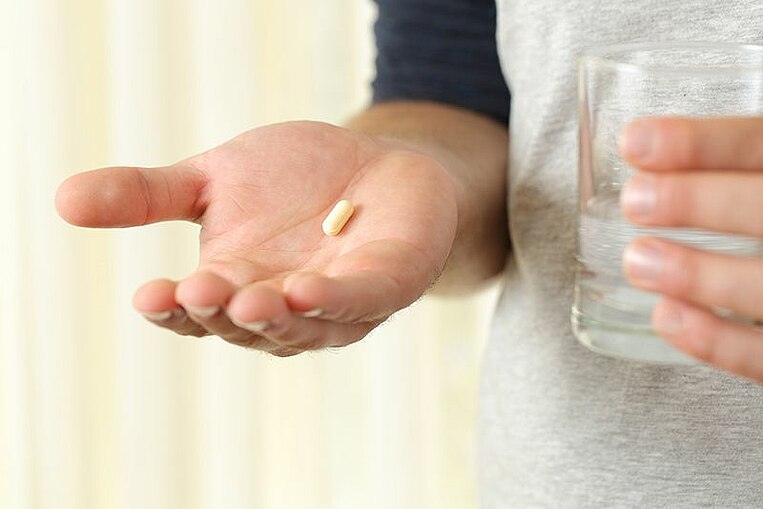 Hand auf der eine Kapsel liegt und in der anderen Hand wird ein Wasserglas gehalten Hand auf der eine Kapsel liegt und in der anderen Hand wird ein Wasserglas gehalten