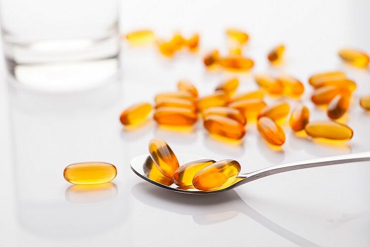 Omega-3-Fettsäure Kapseln auf einem Löffel und daneben zerstreut Omega-3-Fettsäure Kapseln auf einem Löffel und daneben zerstreut