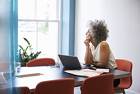 Frau sitzt mit einem Laptop am Tisch und arbeitet