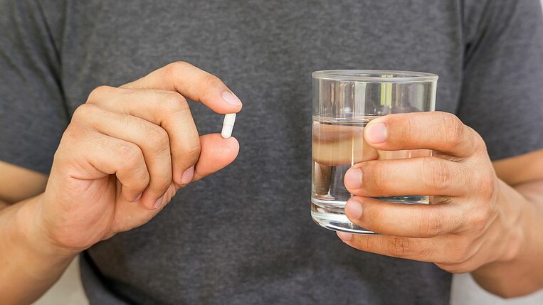Person hält eine Tablette in er einen, und ein Glas Wasser in der anderen Hand Person hält eine Tablette in er einen, und ein Glas Wasser in der anderen Hand