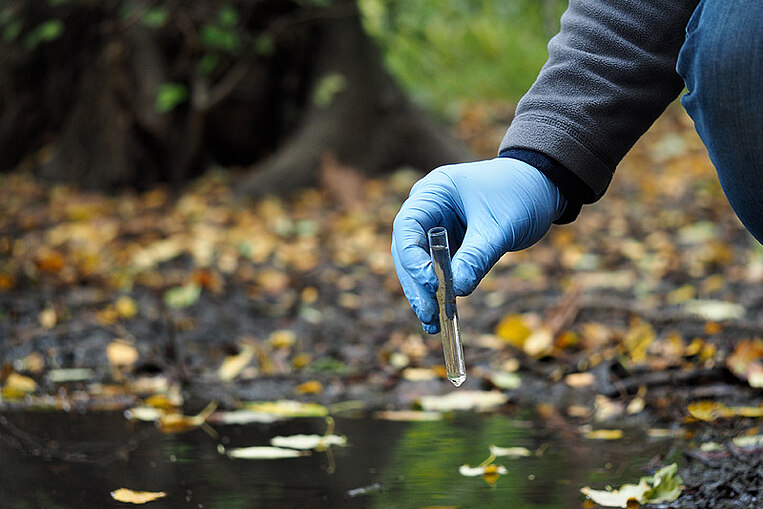 Eine Person nimmt Proben aus einem Gewässer Eine Person nimmt Proben aus einem Gewässer