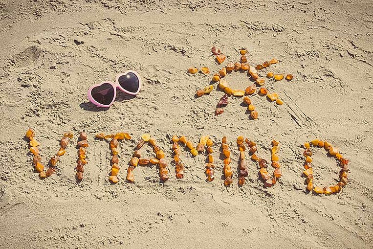 Inschrift Vitamin D und eine Sonne auf einen Sand gelegt Inschrift Vitamin D und eine Sonne auf einen Sand gelegt