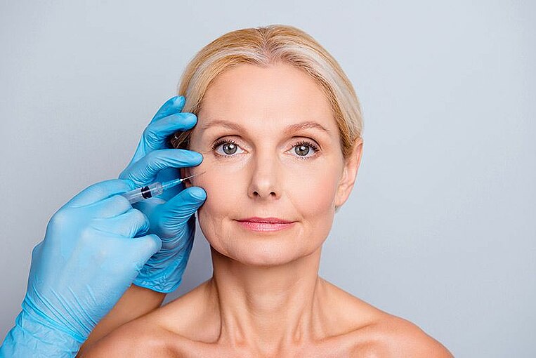 Spritze, die bei einer Frau im Gesicht unter dem Auge angesetzt wird Spritze, die bei einer Frau im Gesicht unter dem Auge angesetzt wird
