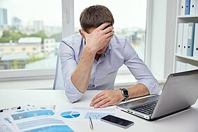 A man sitting in front of a laptop holding his head.