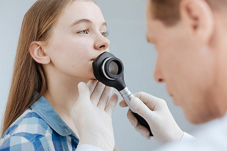 Arzt untersucht das Gesicht ein junges Mädchens mit einem speziellen Instrument  Arzt untersucht das Gesicht ein junges Mädchens mit einem speziellen Instrument