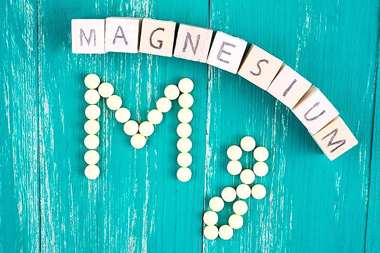 Hölzerne Würfel mit der Aufschrift Magnesium und Mg aus Tabletten gelegt Hölzerne Würfel mit der Aufschrift Magnesium und Mg aus Tabletten gelegt
