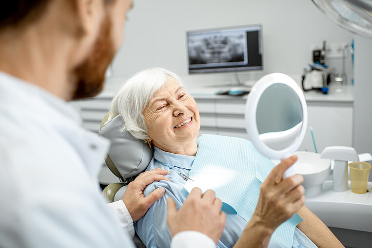 Donna anziana che guarda nello specchio il suo nuovo impianto dentale Donna anziana che guarda nello specchio il suo nuovo impianto dentale