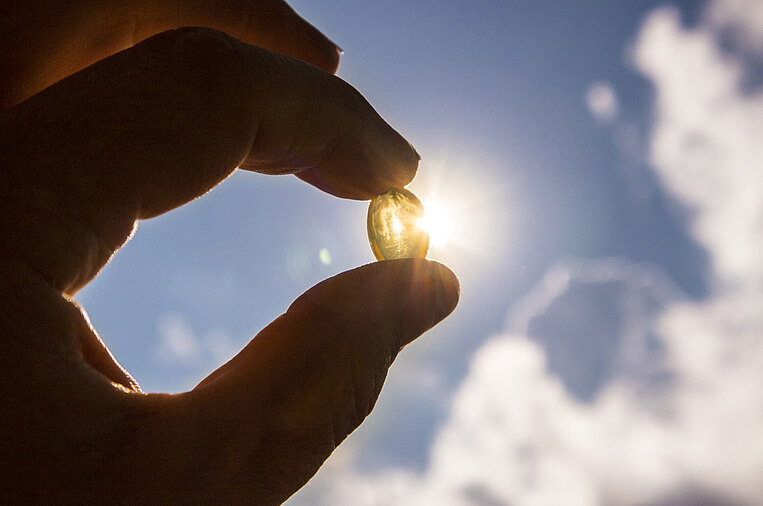 Person hält eine Vitamin-D-Kapsel gegen das Sonnenlicht Person hält eine Vitamin-D-Kapsel gegen das Sonnenlicht