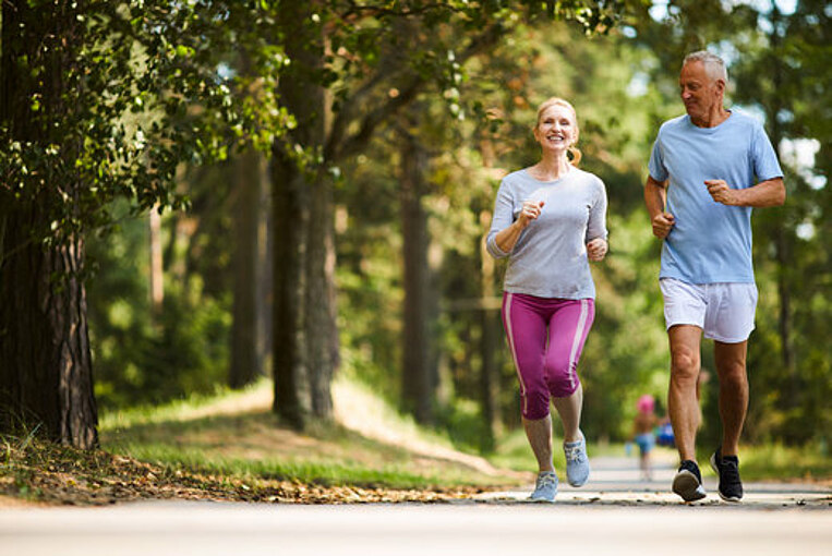 Eine Frau und ein Mann joggen gemeinsam durch einen Wald Eine Frau und ein Mann joggen gemeinsam durch einen Wald