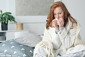 Woman suffering from a cold, sitting in bed holding tissues 