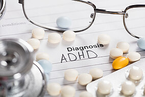 Glasses and tablets lying on a sheet of paper with the heading: Diagnosis ADHD.