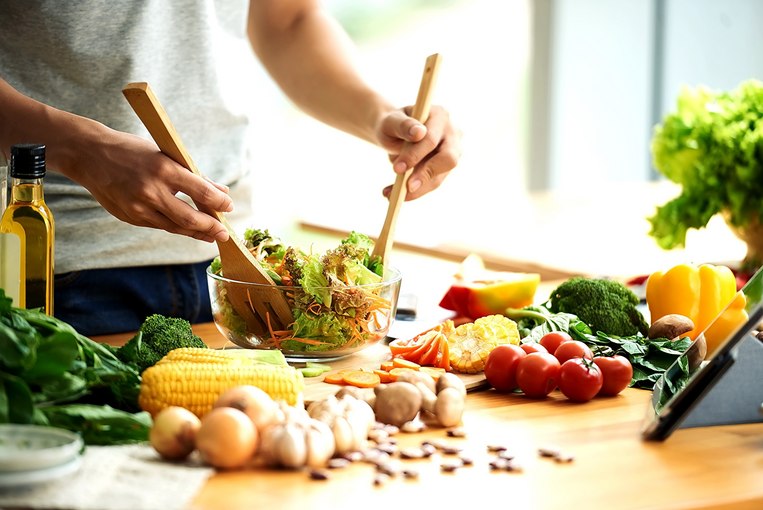 Person bereitet gesunden Salat aus frischem Gemüse zu