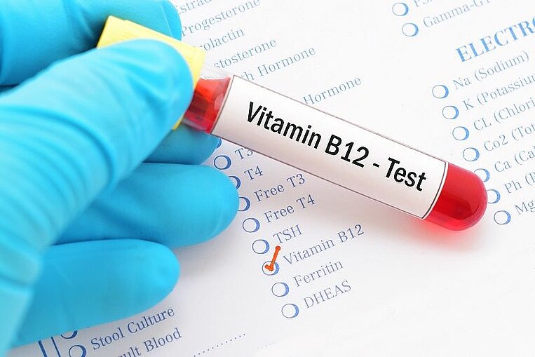 Ampulle mit der Aufschrift "Vitamin B12-Test" wird vor ein Testblatt gehalten Ampulle mit der Aufschrift "Vitamin B12-Test" wird vor ein Testblatt gehalten