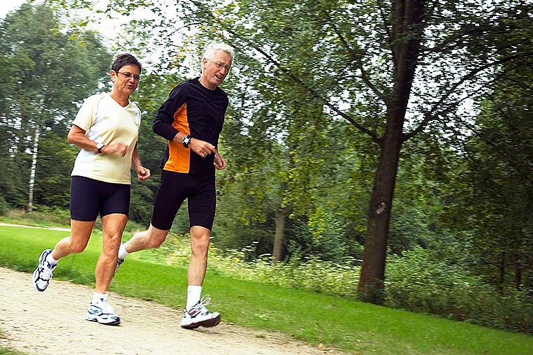 Elderly man and woman jogging in the park Ältere Frau und älterer Mann joggend im Park