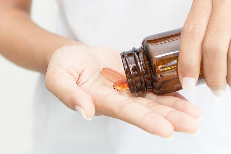 Donna che si versa capsule nella mano da un flacone Donna che si versa capsule nella mano da un flacone