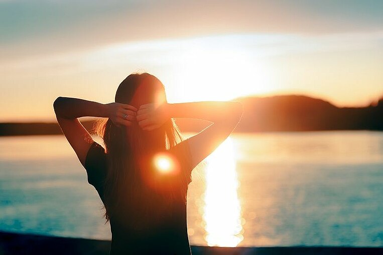 Frau steht am Wasser und betrachtet einen Sonnenuntergang Frau steht am Wasser und betrachtet einen Sonnenuntergang
