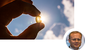Person hält eine Vitamin-D-Kapsel gegen das Sonnenlicht Person hält eine Vitamin-D-Kapsel gegen das Sonnenlicht