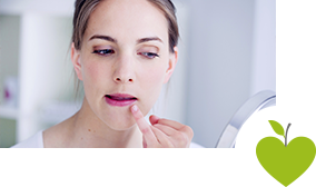 Frau schaut in einen Spiegel und untersucht ihren Lippenherpes Frau schaut in einen Spiegel und untersucht ihren Lippenherpes