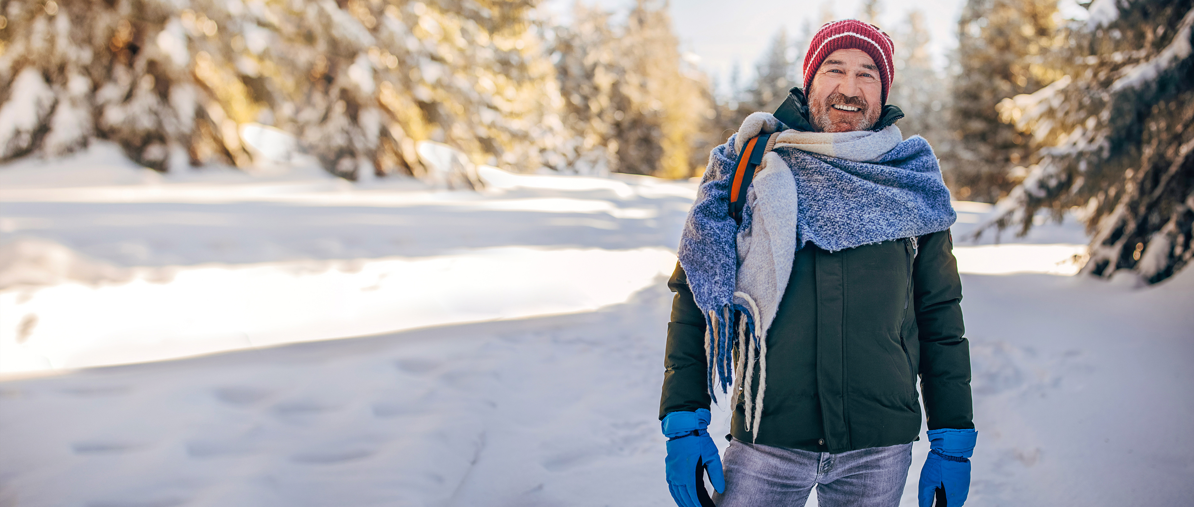 A middle-aged man stands smiling and warmly dressed in a snowy forest